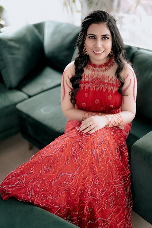 Smiling Young Model in Embroidered Red Dress with Long Sleeves Sitting on Green Sofa