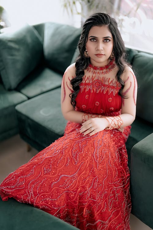 Beautiful Young Woman in an Elegant Red Dress with Long Sleeves Sitting on a Green Sofa