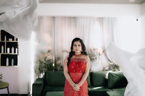 Model in an Embroidered Red Dress Standing in a Living Room Among Flowing White Curtains