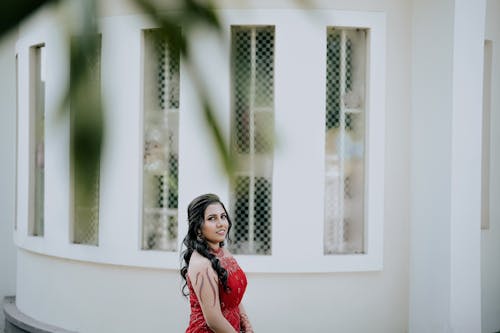 Smiling Model in a Red Dress with Embroidered Sleeves Walking Near the House