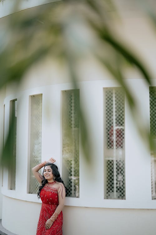 Young Woman in an Embroidered Red Dress Posing in Front of the House Windows