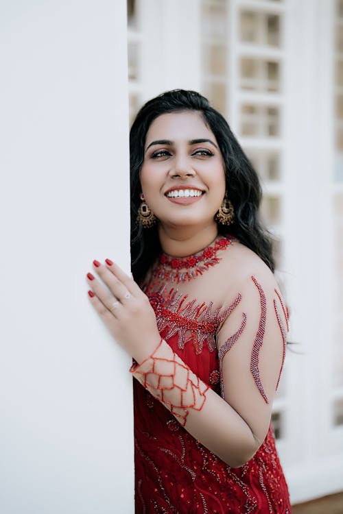 Smiling Bride in a Red Wedding Dress Hugging the Wall of the House