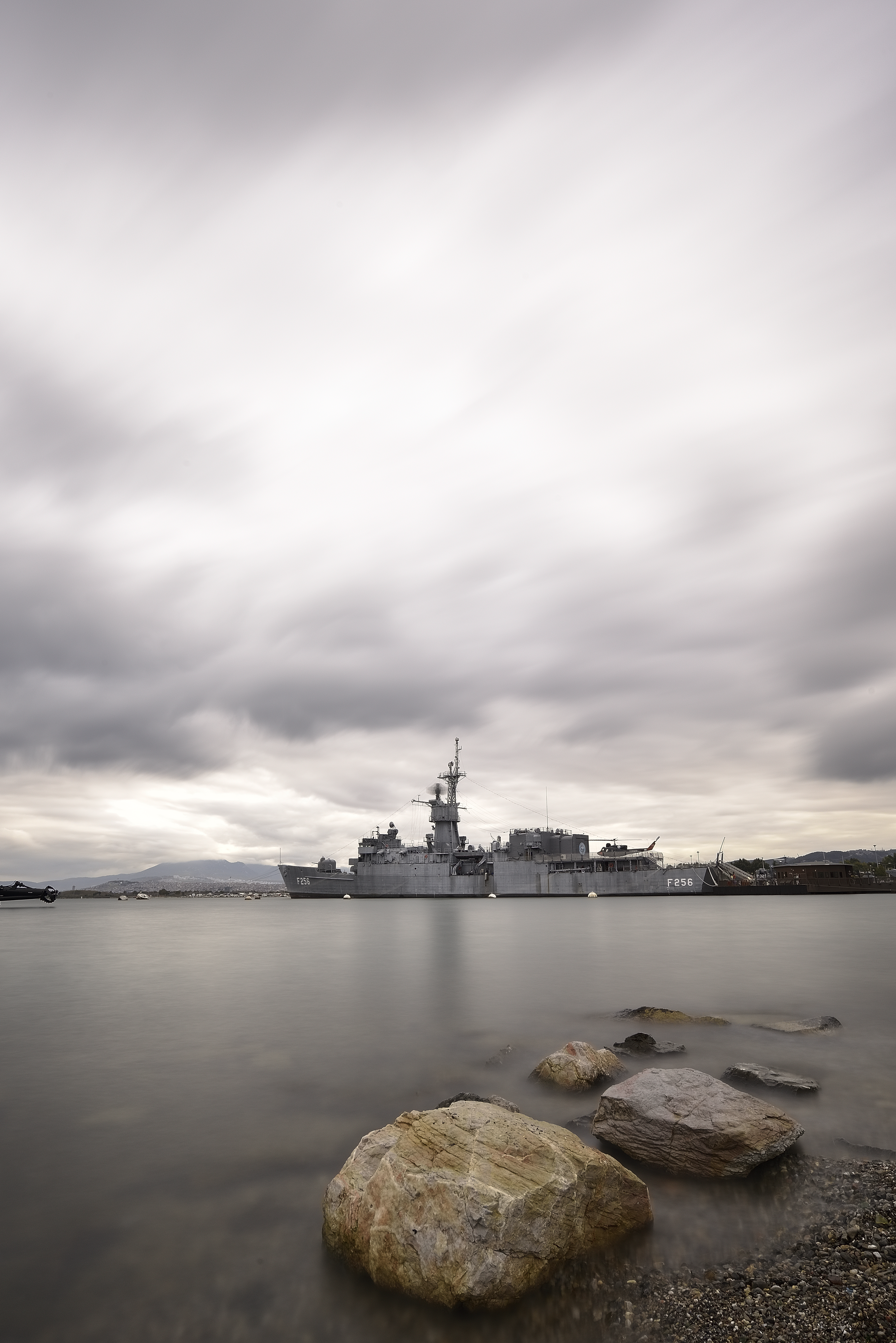 Warship anchored near İzmir coast under dramatic cloudy skies, showcasing serene maritime landscape.