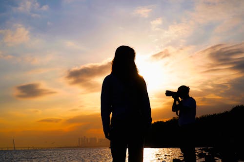 Free Silhouettes of a Man and Woman Standing on a Shore at Sunset Stock Photo