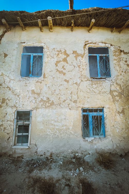 Free Deserted rustic house facade with distinctive blue window frames and thatched roof. Stock Photo