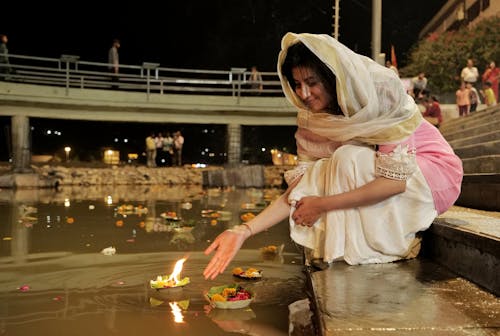 Woman in Traditional Clothing Putting a Candle in a River 