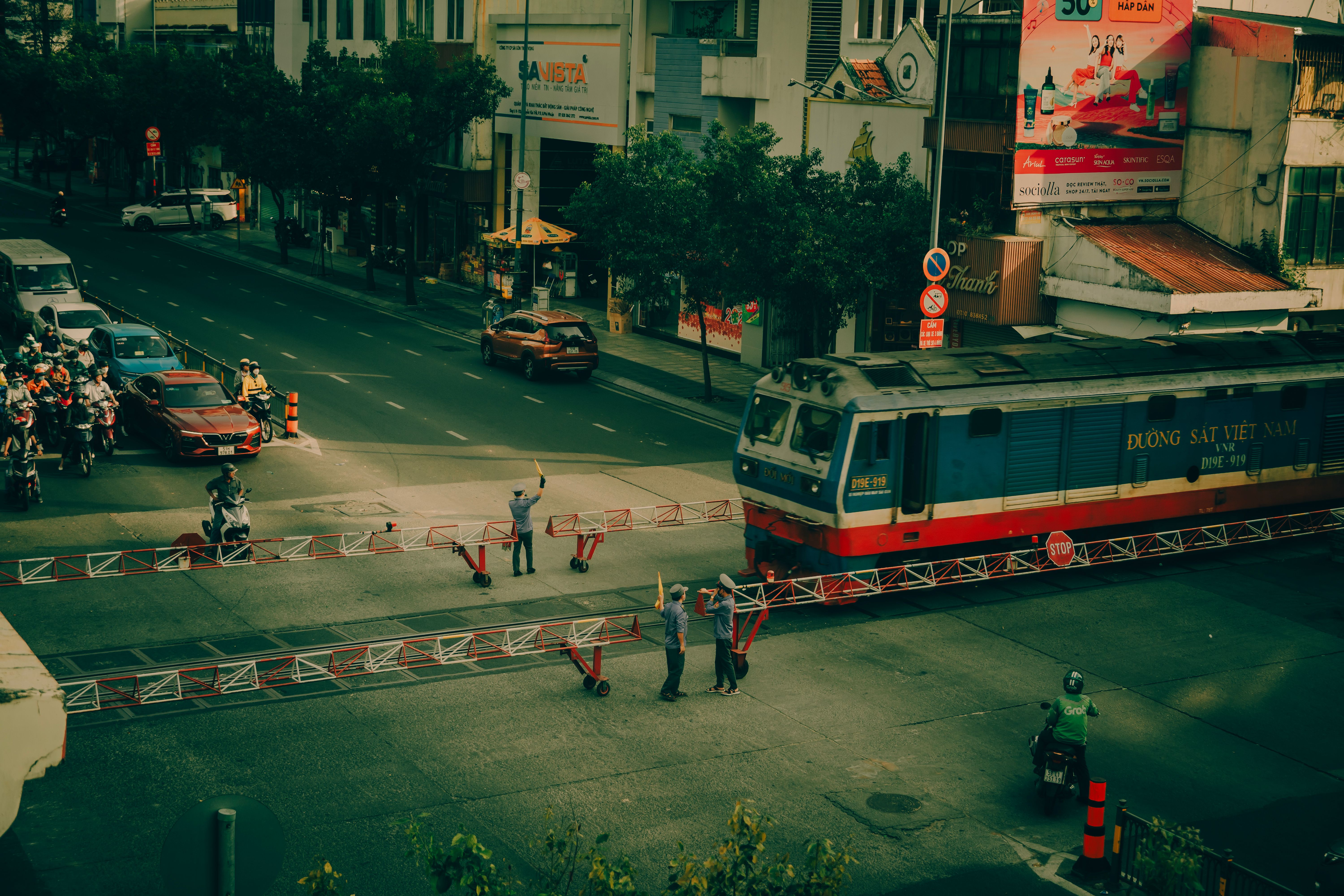 A Vietnamese city street showing a train crossing, with visible signage and city traffic.