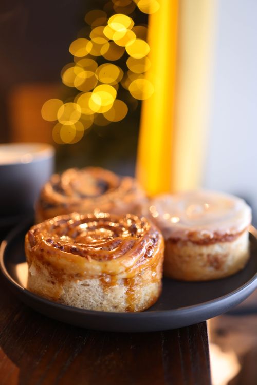 Free Close-up of sweet cinnamon buns on a plate with a festive bokeh background, perfect for holiday-themed visuals. Stock Photo
