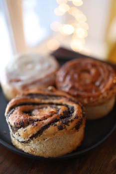 Tasty homemade sweet rolls featuring cinnamon and poppy seeds on a black plate indoors.
