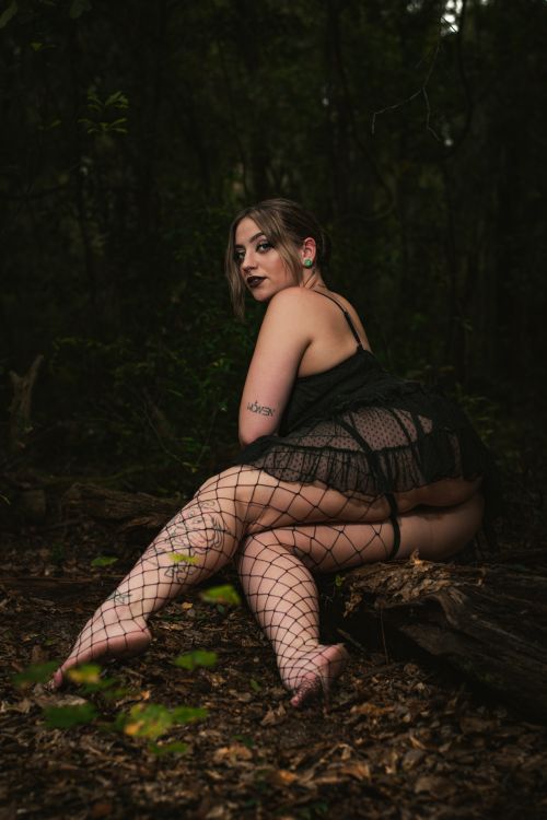 Free Model in black lace and fishnet poses in forest setting, showcasing gothic fashion. Stock Photo