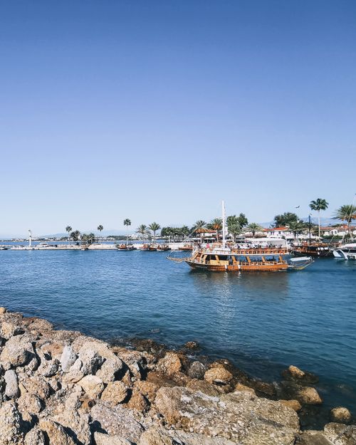 Free A scenic view of boats in a coastal harbor featuring clear blue skies and palm trees lining the shore. Stock Photo