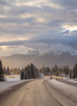 Snowy road leading towards majestic mountains in Banff, Alberta, Canada.