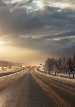 Enchanting winter view of a road in Banff National Park with mountains and a dramatic sky.