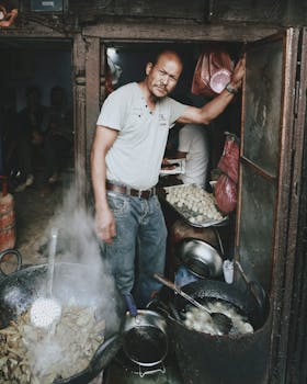 Asian street vendor cooking traditional food outdoors with rustic charm and steaming pots.