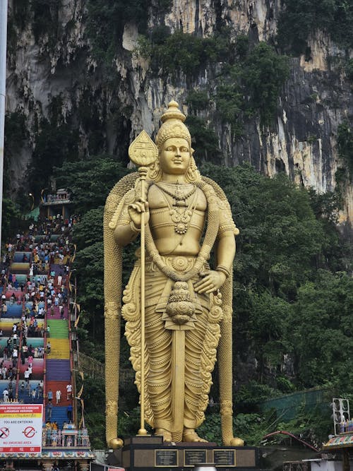 Lord Murugan Sculpture by a Rocky Mountain, and Climbing Tourists