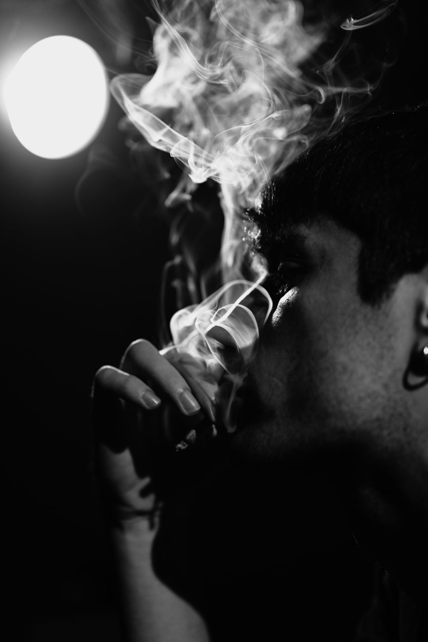 Artistic black and white portrait of a man exhaling smoke with dramatic lighting.