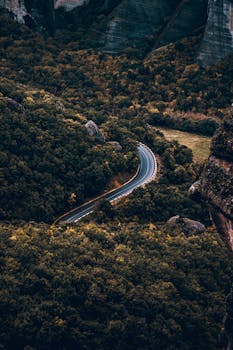 Stunning aerial shot of a winding road through dense forest in a mountainous region.