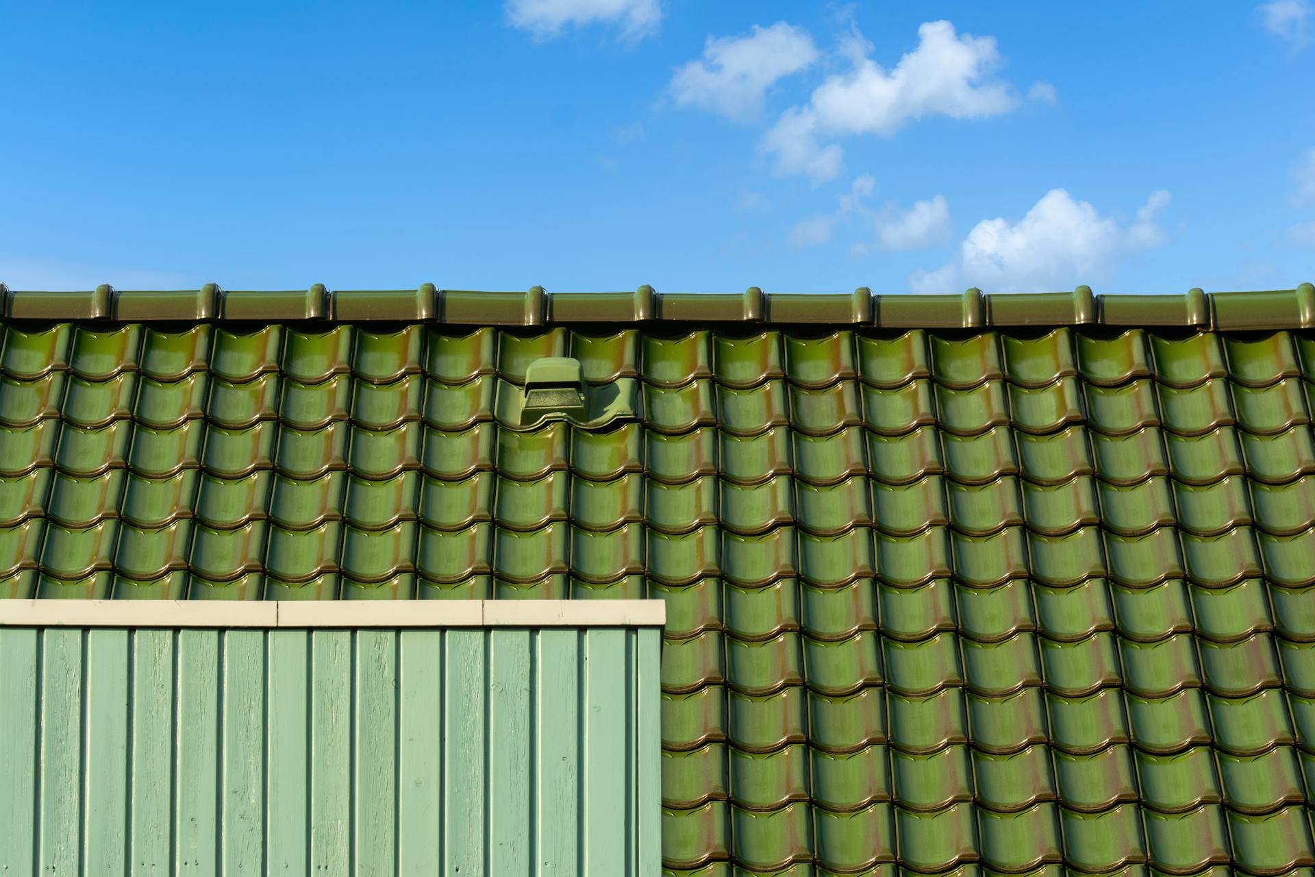 Closeup of a green tiled roof under a bright blue sky, capturing architectural detail and color contrast.