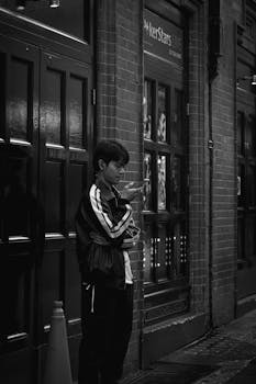 A young adult uses their smartphone while leaning against a brick building in an urban setting.