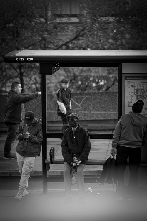 Free Black and white image of people waiting at a city bus stop, capturing urban street life. Stock Photo