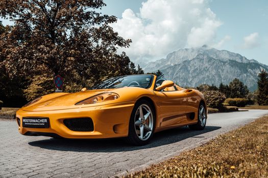 A sleek yellow sports convertible car on a mountain road with a scenic backdrop.