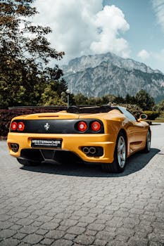 A sleek yellow Ferrari parked on a scenic road with mountains in the background.
