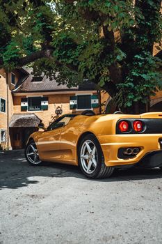 Elegant yellow sports car parked near a rural house under a lush tree.