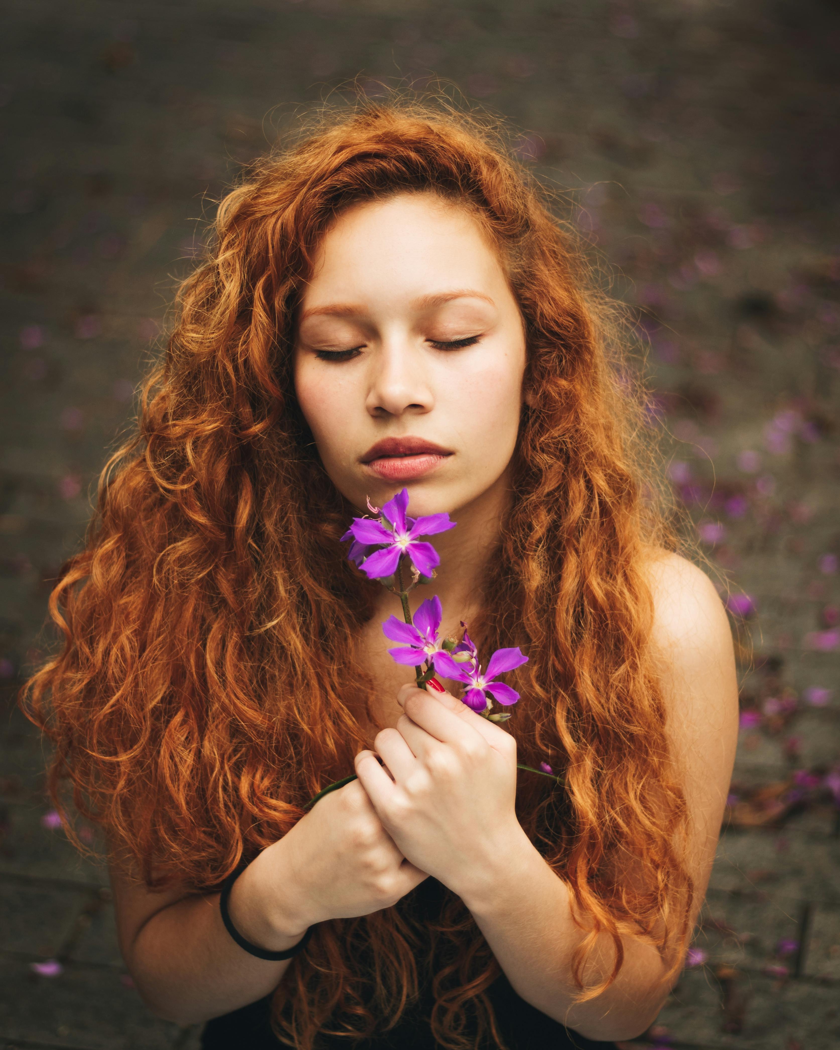 一个美丽的红发女人闭着眼睛，在宁静的时刻拿着一束紫色的花