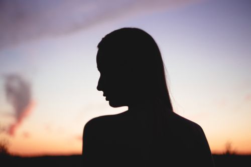 Free A serene silhouette of a woman against a vibrant sunset sky, capturing the tranquility of nature. Stock Photo