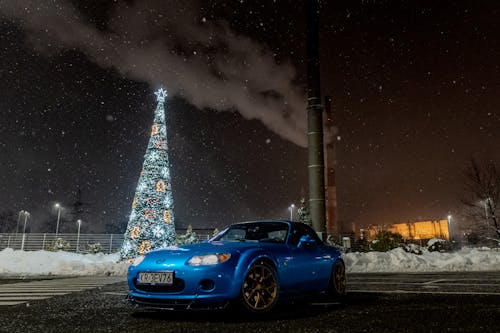 A blue sports car parked in front of a christmas tree
