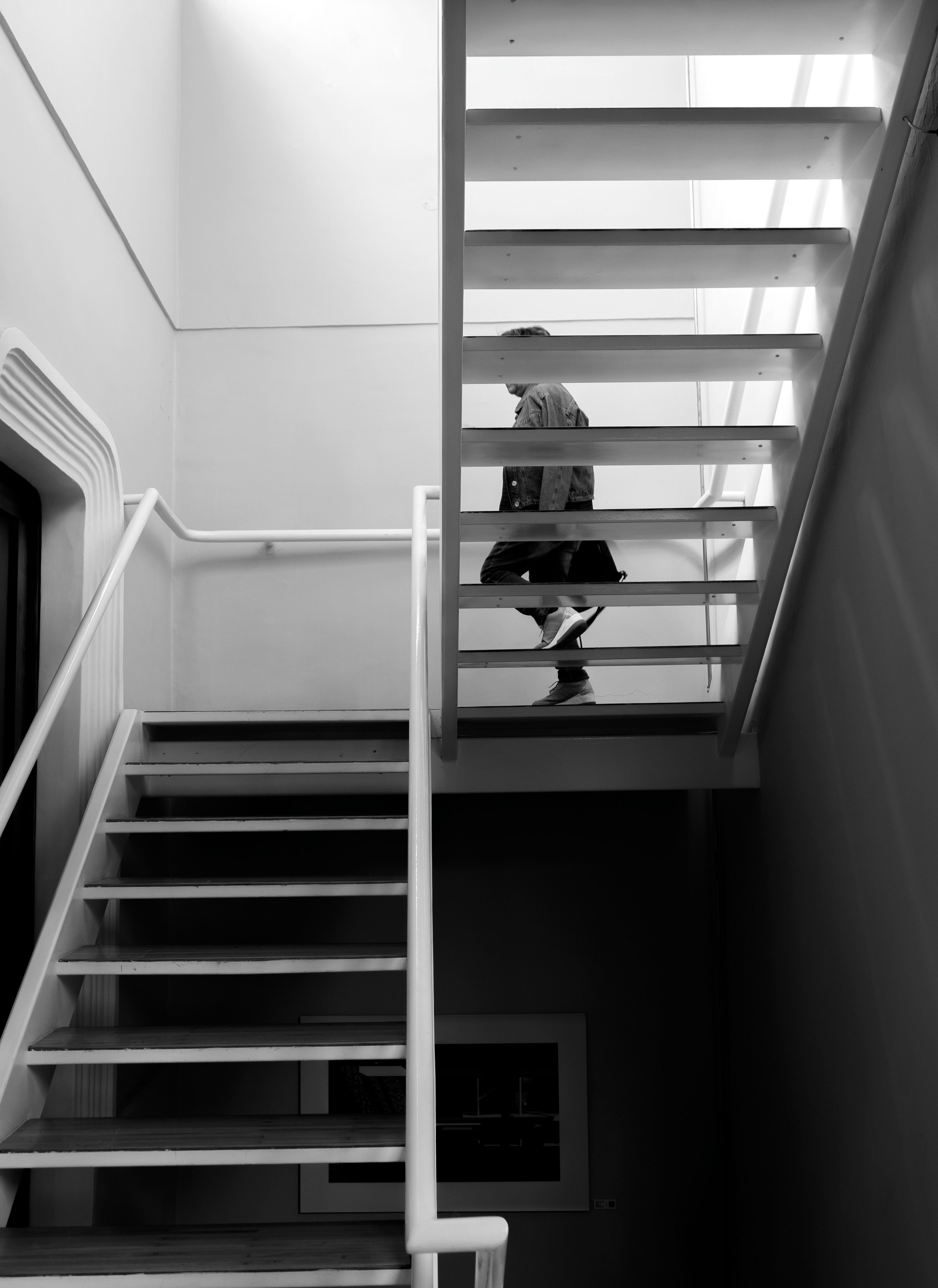 Black and white image of a person walking down a modern staircase indoors.