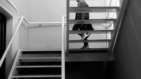 Black and white image of a person walking down a modern staircase indoors.