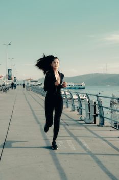 Young woman running along a sunny pier near the sea, showcasing fitness and outdoor activity.