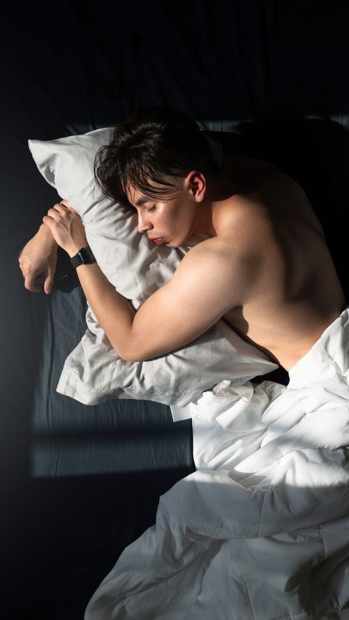 Free A young muscular man sleeping topless in bed captured from above, embracing relaxation. Stock Photo