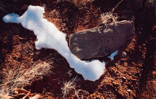 Free A close-up view of snow melting on red desert soil, revealing rocks and dry grass. Stock Photo
