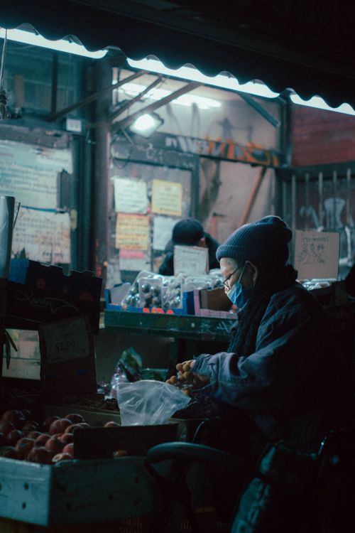 Free A vendor wearing a face mask handles fruits at a bustling night market in a city. Stock Photo