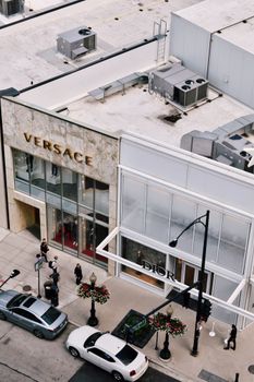 High-angle shot of Versace and Dior stores on a bustling city street with pedestrians and cars.