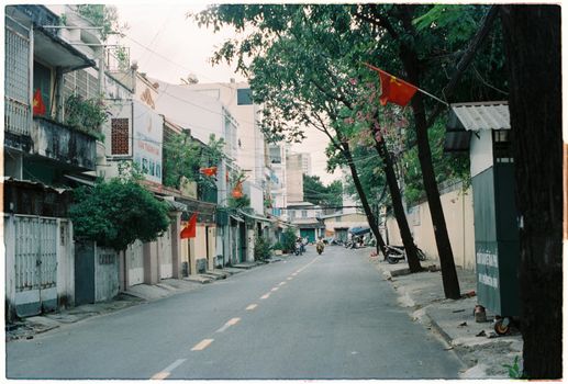 Quiet urban street lined with flags and trees, showcasing residential architecture in an Asian city.