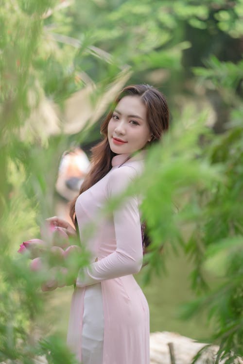 Model in a Pink Ao Dai Dress with a Slit and White Pants Among the Leaves