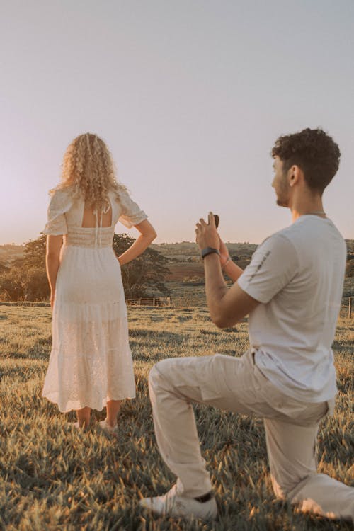 Man Taking Pictures of Woman in White Dress on Grassland