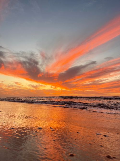 Free Vibrant sunset reflecting over calm waves and a sandy beach. Stock Photo