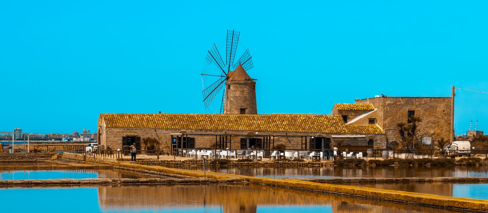 Stunning view of a historic windmill at Trapani Salt Works, Sicily, with mirror-like reflections.