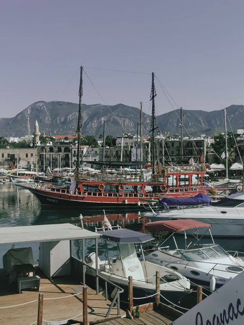 Free Explore a picturesque harbor with a classic wooden ship docked alongside modern yachts against mountain scenery. Stock Photo