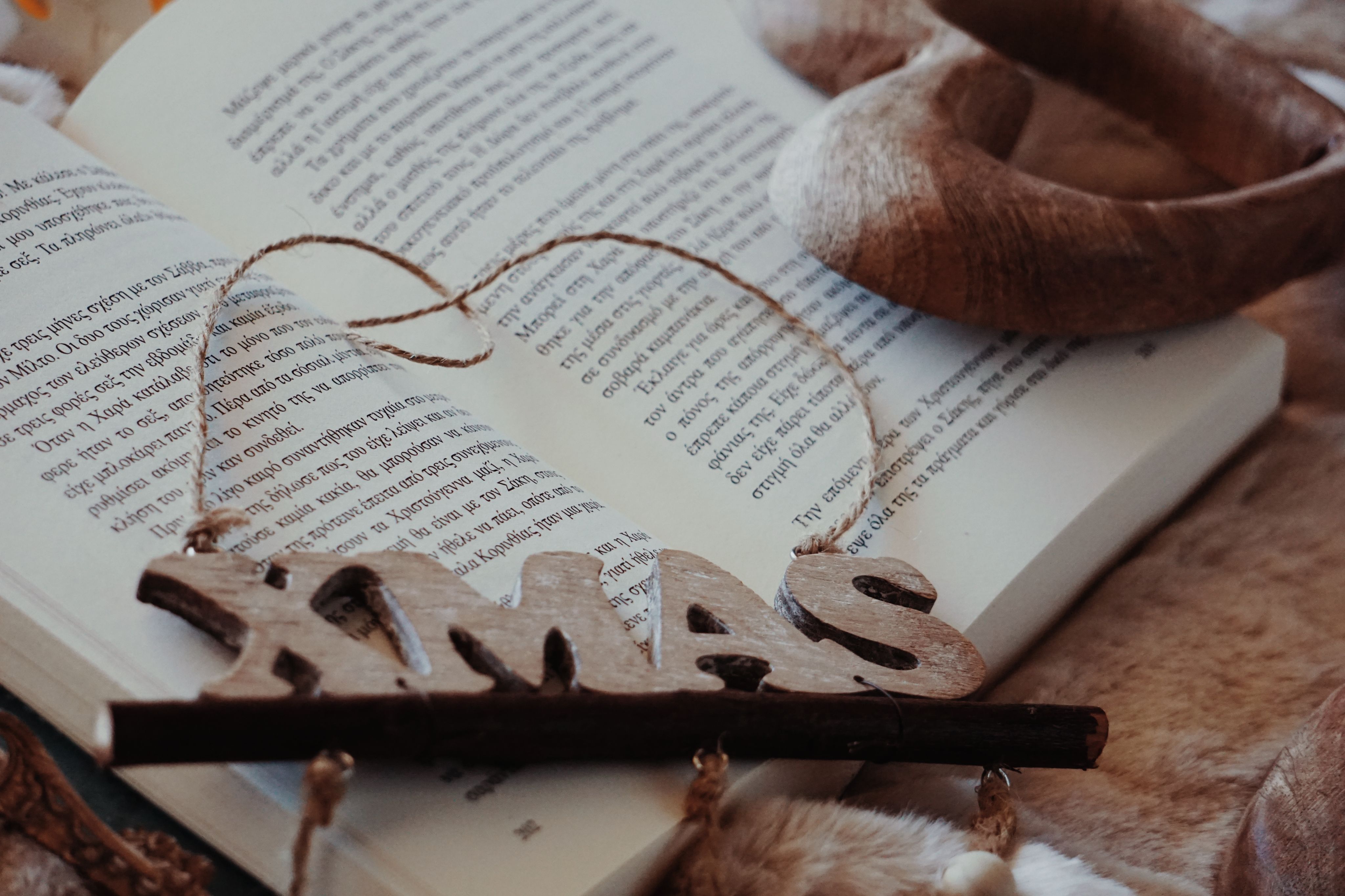Rustic wooden Christmas decoration resting on an open Greek book, creating a cozy holiday atmosphere.