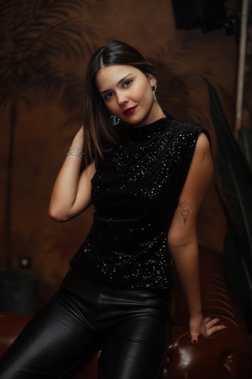 Model in Glittery Sleeveless Black Blouse and Leather Pants Posing by the Sofa