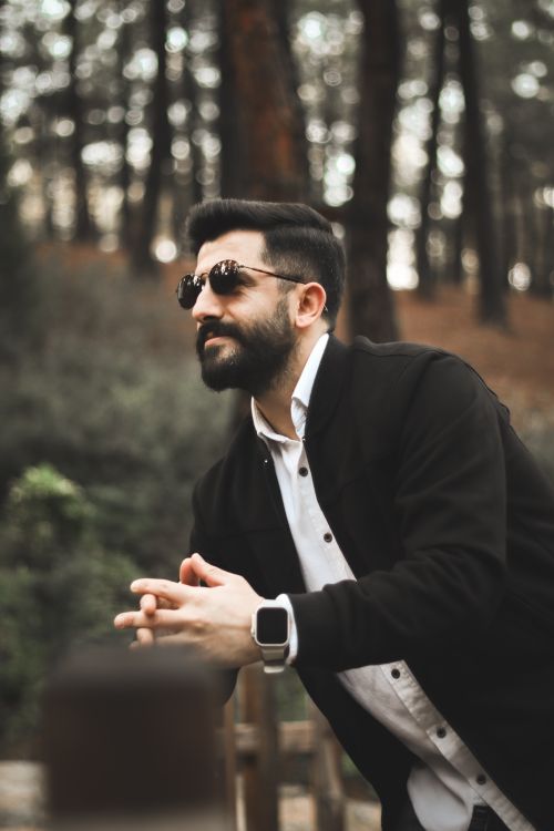 Free Man with sunglasses and beard in a forest setting, exuding a casual yet elegant style. Stock Photo
