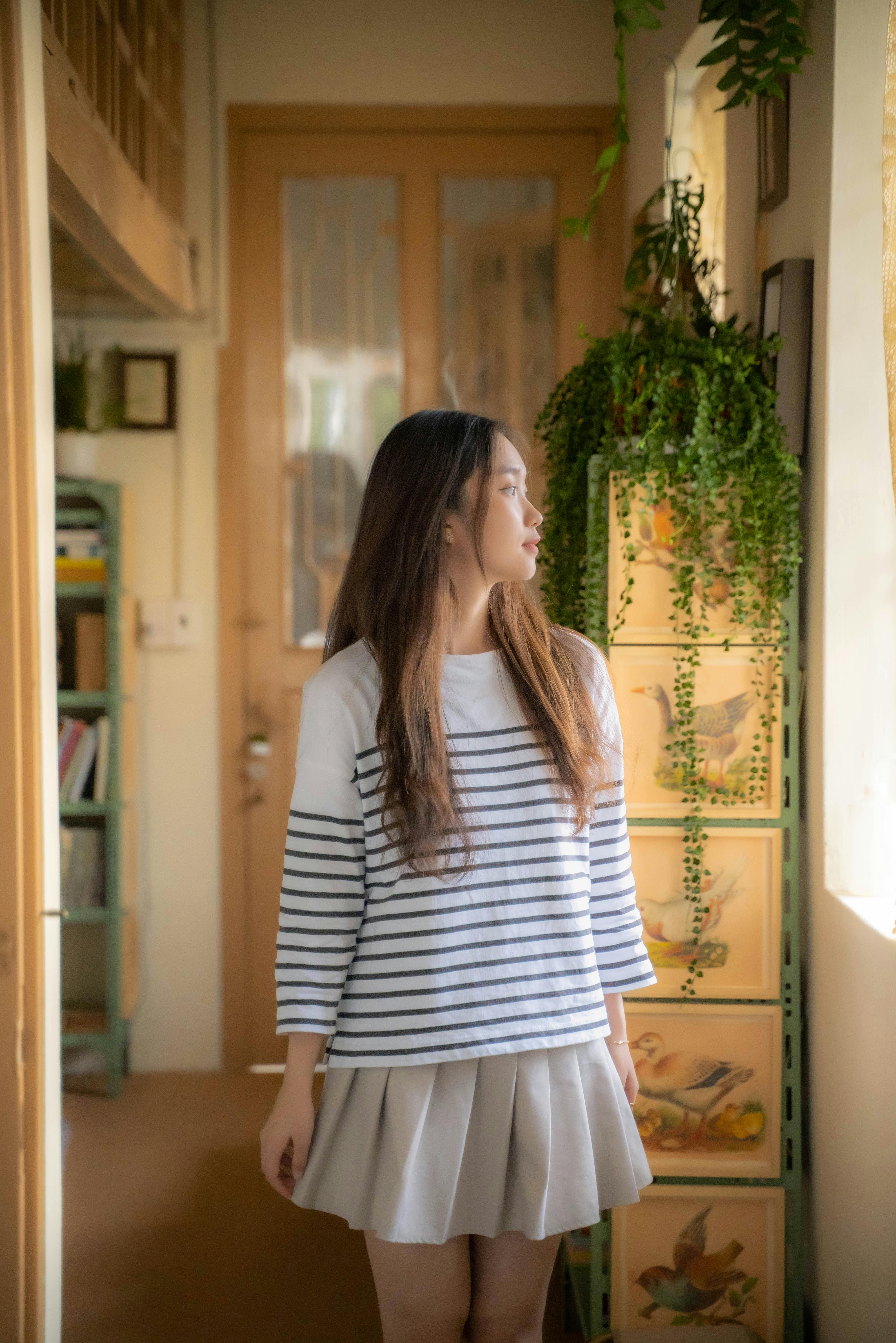 Young Woman in a White Striped Sweater and Pleated Mini Skirt Looking Out  the Window · Free Stock Photo