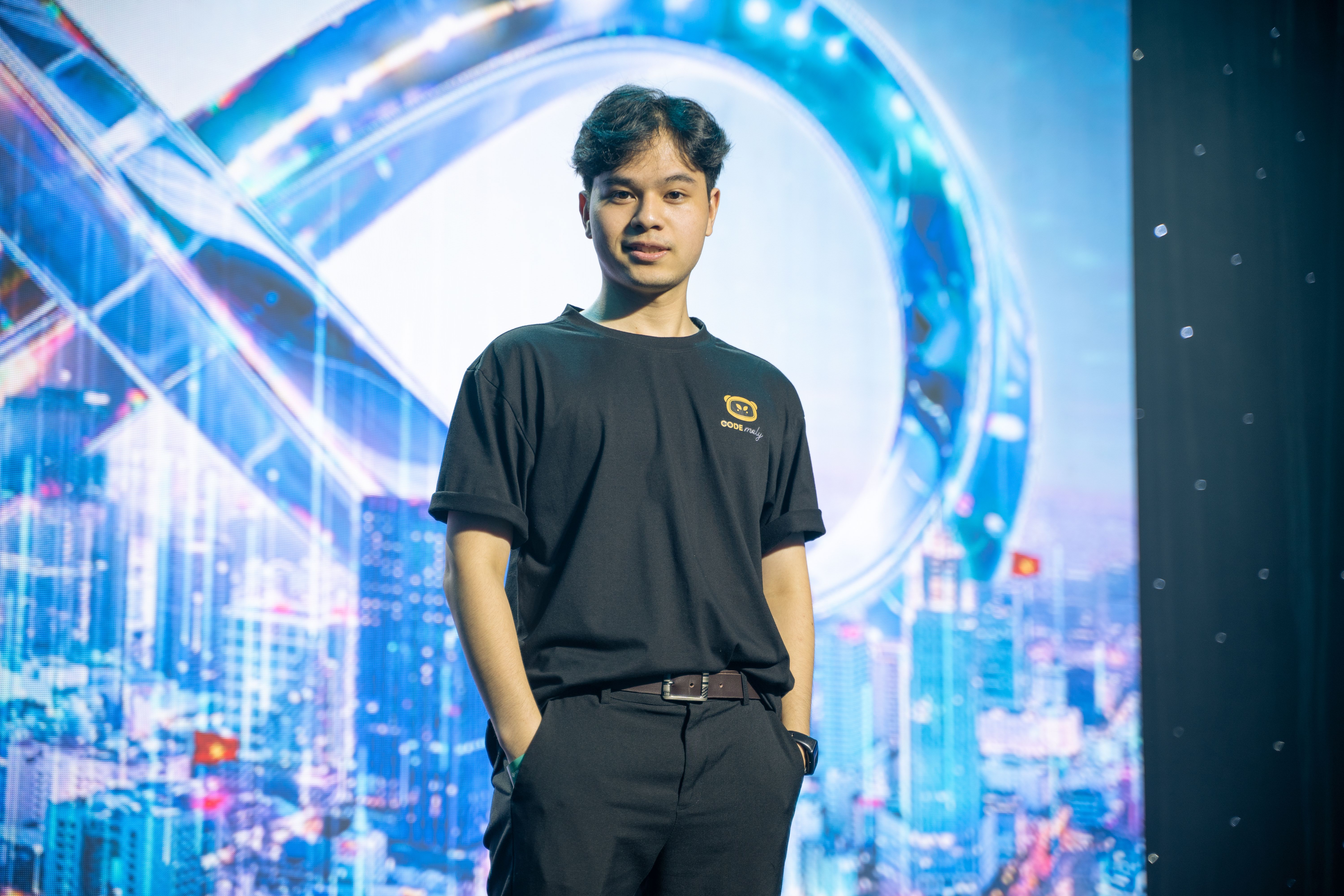 Asian man in black t-shirt stands confidently in modern indoor setting.