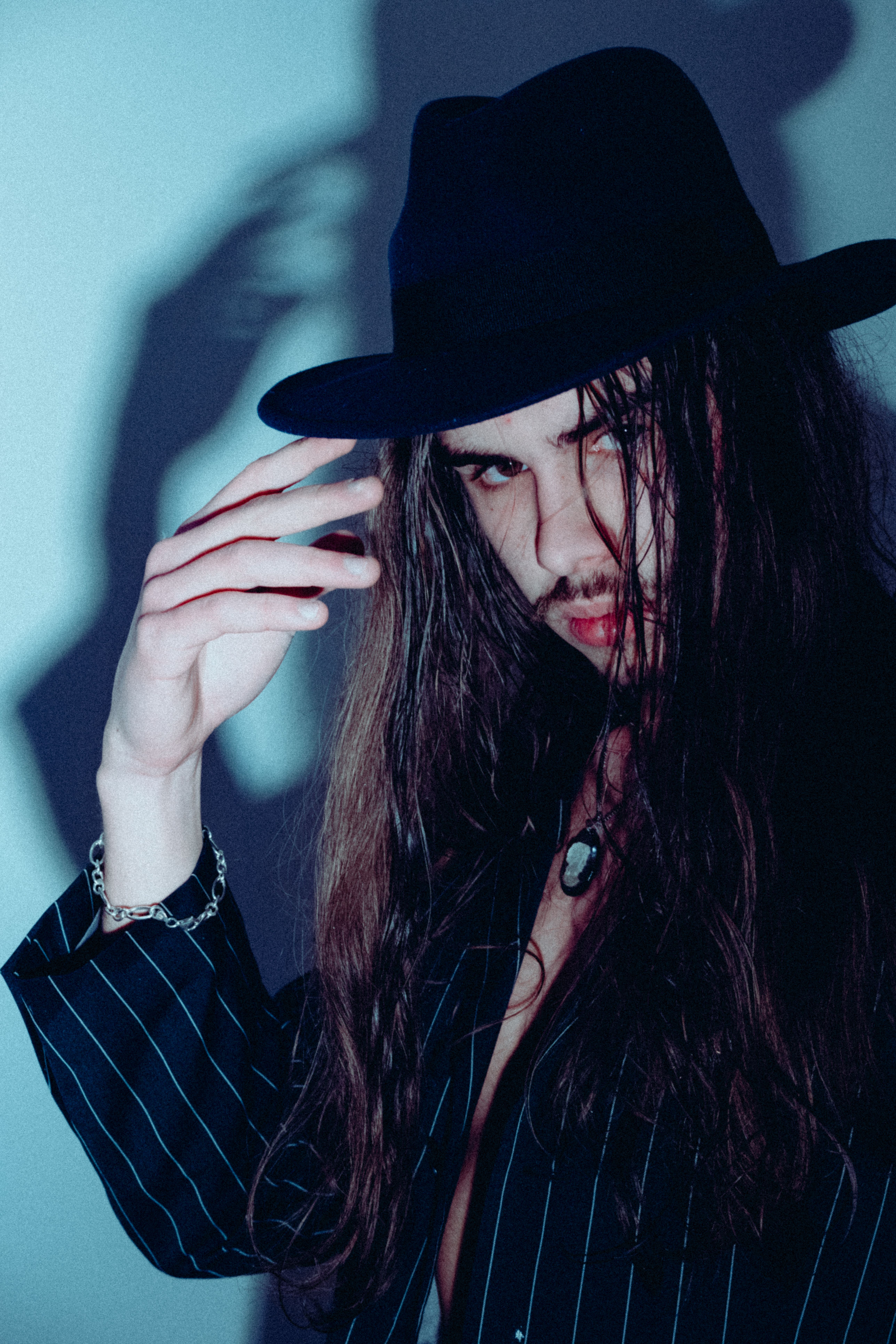 Fashionable adult man in hat striking a pose, creating dramatic shadows.