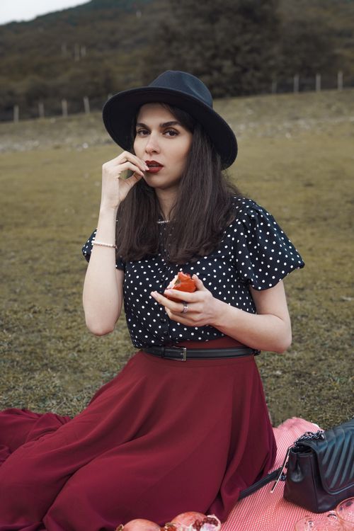 Free Woman in polka dot blouse and red skirt enjoys fruit during outdoor picnic. Stock Photo